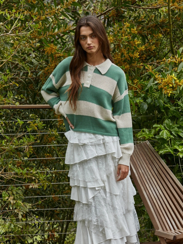 Woman wearing a green and white striped sweater with a layered white dress, standing outdoors.