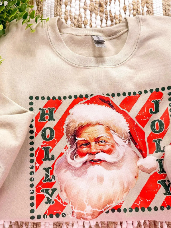 Beige sweatshirt with a graphic of Santa Claus and 'Holly Jolly' text on a neutral background.