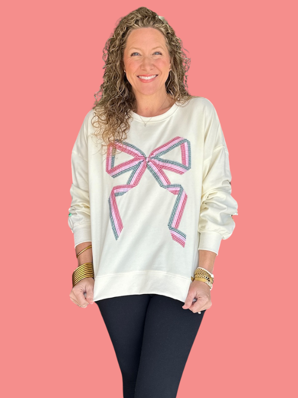 Woman wearing a white sweatshirt with a colorful bow design on a pink background