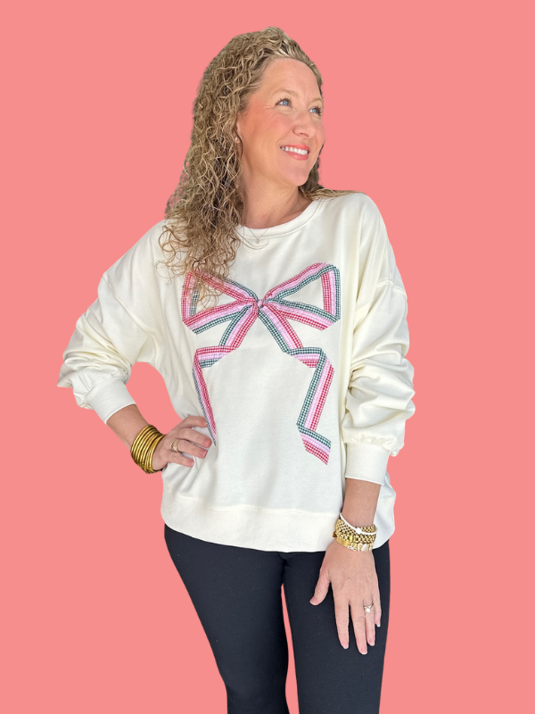 Woman wearing a white sweatshirt with a colorful bow design on a pink background