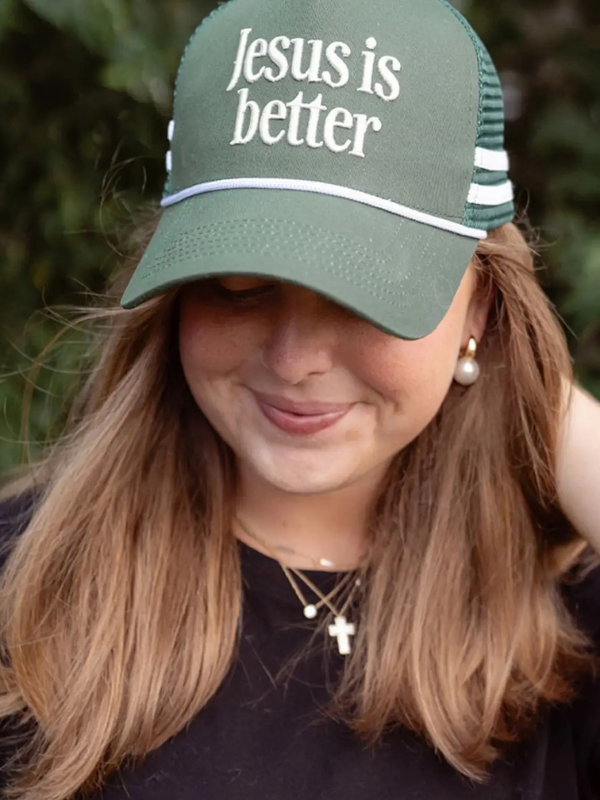 Person wearing a green cap with 'Jesus is better' text, outdoors.