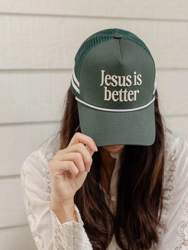 Person wearing a green cap with 'Jesus is better' text against a neutral background