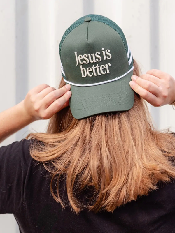 Person wearing a green cap with 'Jesus is better' text against a white background