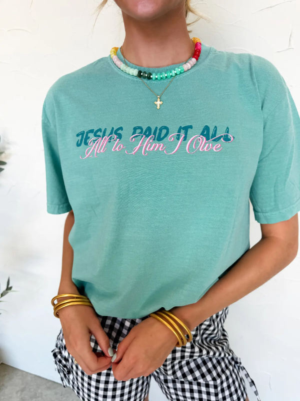 Person wearing a teal t-shirt with text, standing against a white background