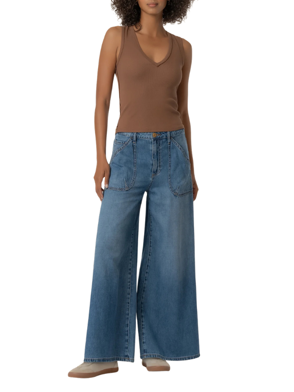 A model wearing a brown sleeveless V-neck top and wide-leg blue denim jeans, standing against a plain white background.