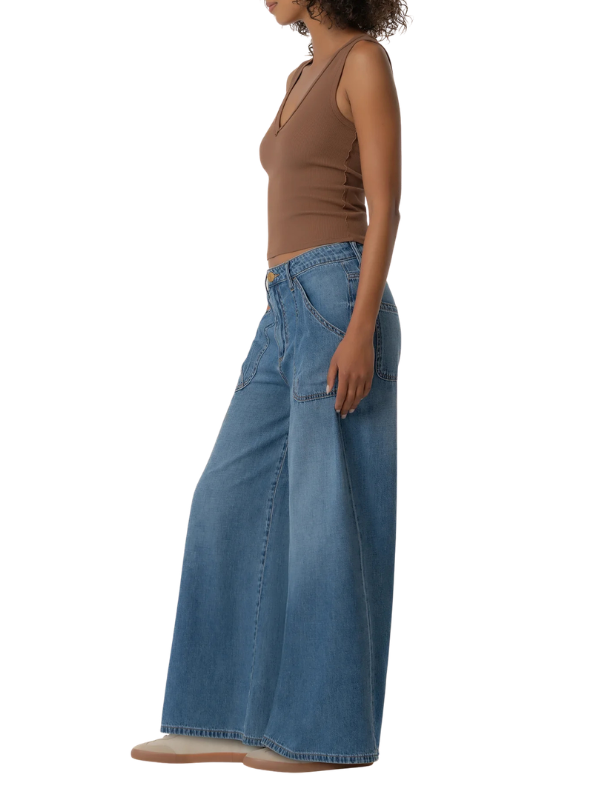 A side-profile view of a model wearing a pair of wide-leg blue denim jeans and a brown sleeveless top against a plain white background.
