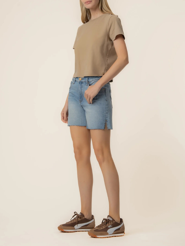 Person wearing a beige top and blue denim shorts on a plain background