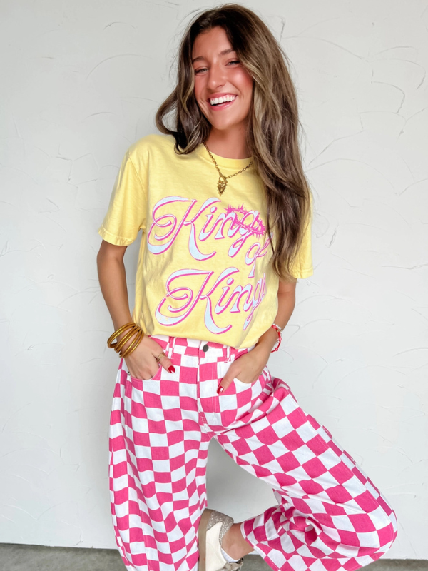 Woman wearing a yellow t-shirt with pink text and pink checkered pants against a white background