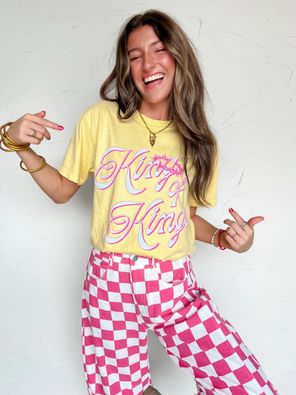 Person wearing a yellow t-shirt with pink text and pink and white checkered pants against a white background