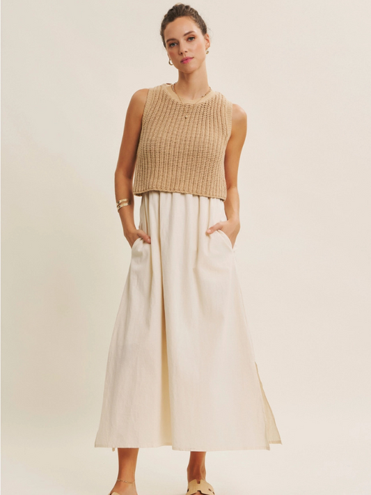 Woman wearing a beige sleeveless top and white pants against a plain background