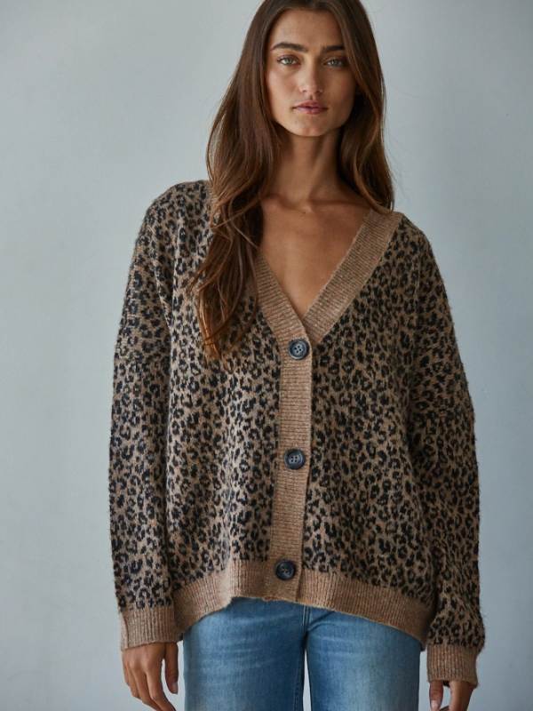 Woman wearing a leopard print cardigan over a beige top with blue jeans against a plain background