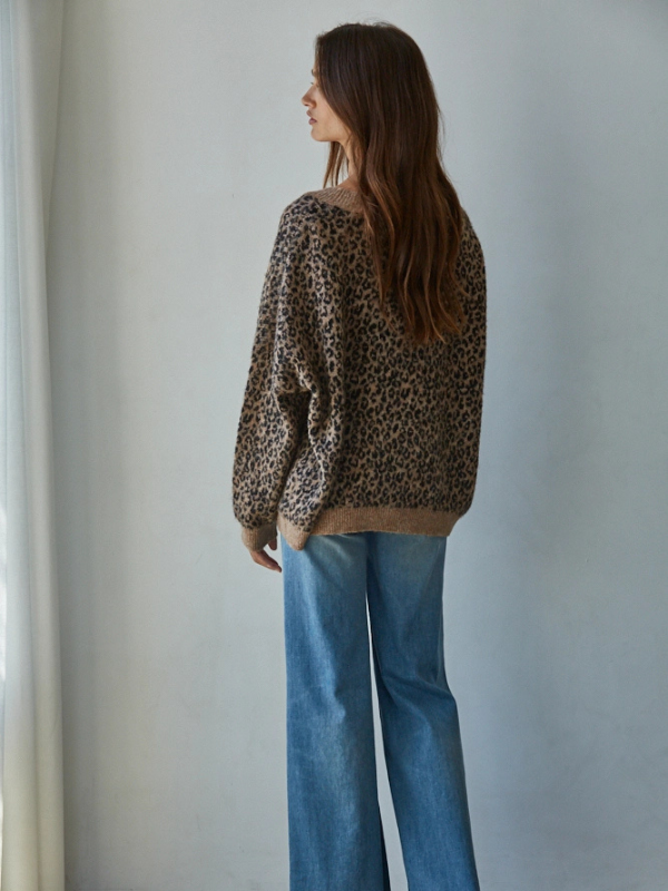 Woman wearing a leopard print sweater and blue jeans against a plain background