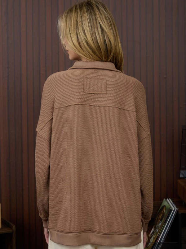 Person wearing a brown textured jacket in front of a wooden paneled wall.