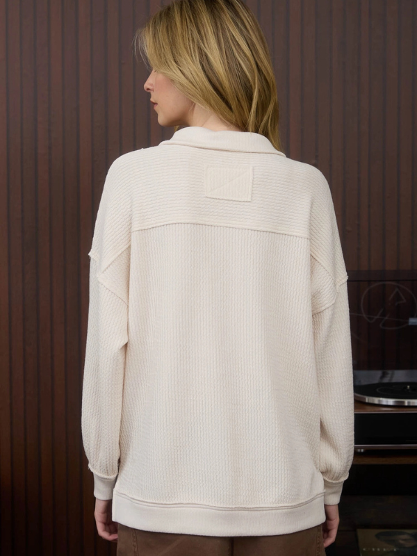 Person wearing a cream-colored jacket in front of a wooden panel background