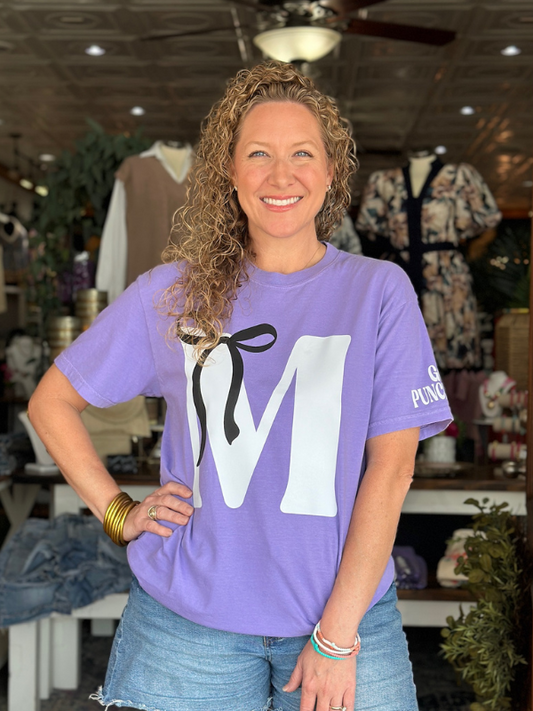 Woman wearing a purple t-shirt with a large white letter 'M' in a store setting