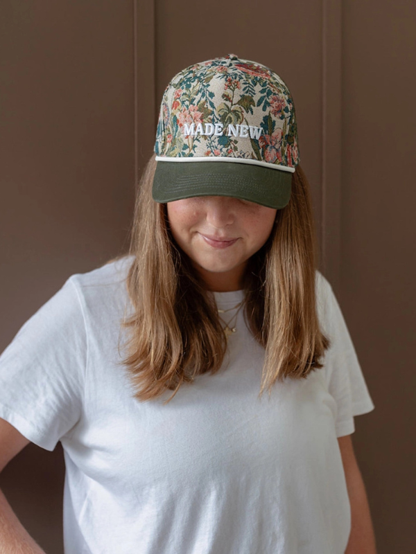 Person wearing a floral cap with 'MADE NEW' text on a plain background