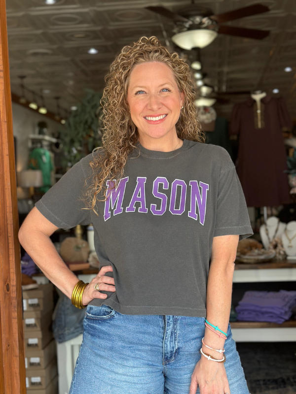 Woman wearing a gray t-shirt with 'MASON' printed in purple inside a store.