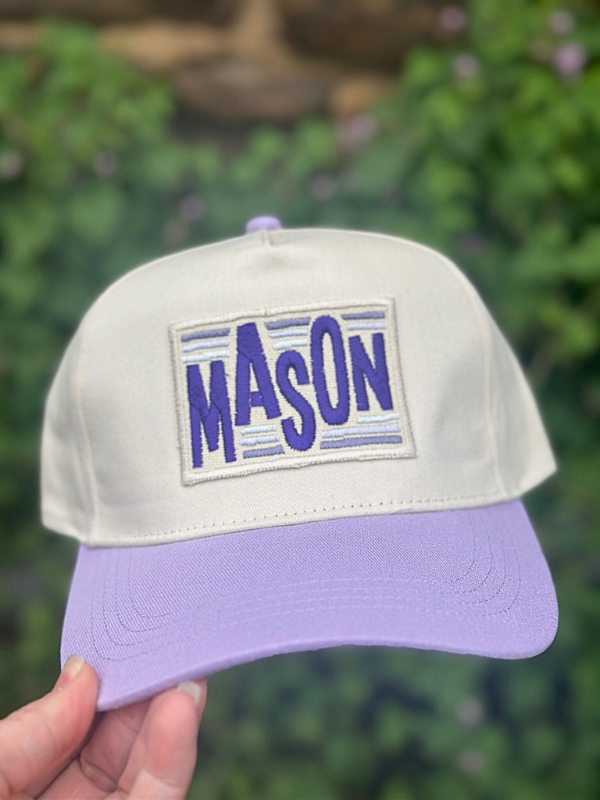 Cap with 'MASON' patch held against a blurred green background