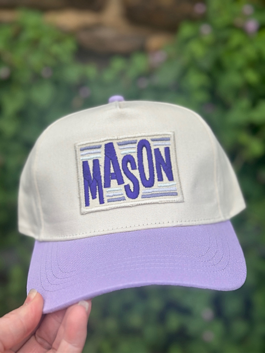 Cap with 'MASON' patch held against a blurred green background