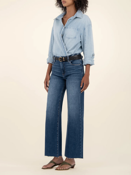Person wearing a light blue denim shirt and dark blue jeans on a beige background