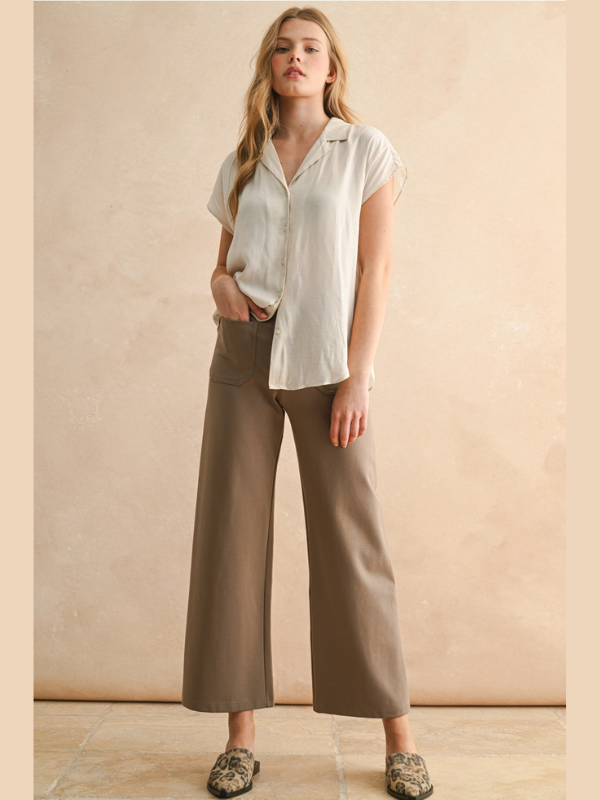 Woman wearing a white shirt and brown wide-leg pants against a beige background