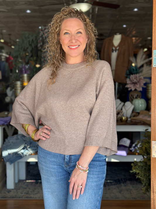 Woman wearing a beige sweater and blue jeans in a store setting