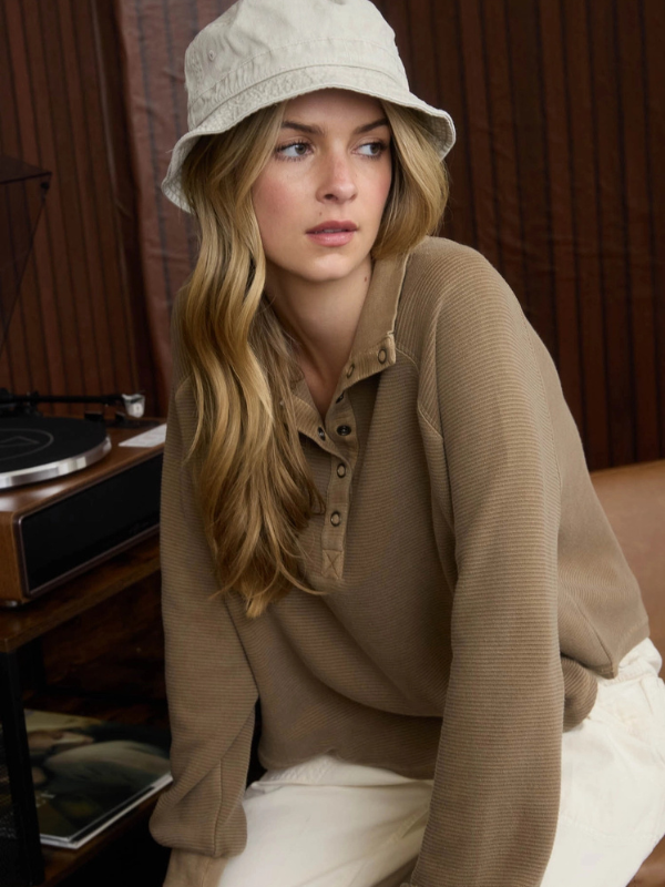Woman wearing a beige hat and sweater sitting in a room with wooden walls.
