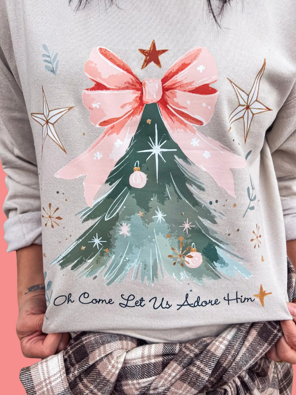 Gray sweatshirt with a Christmas tree design and text held by a person.