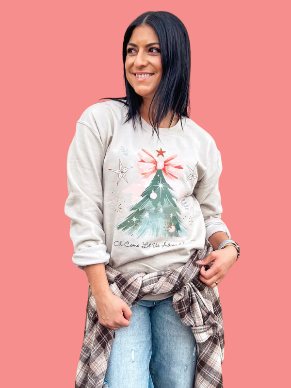 Woman wearing a light gray sweatshirt with a Christmas tree design on a pink background