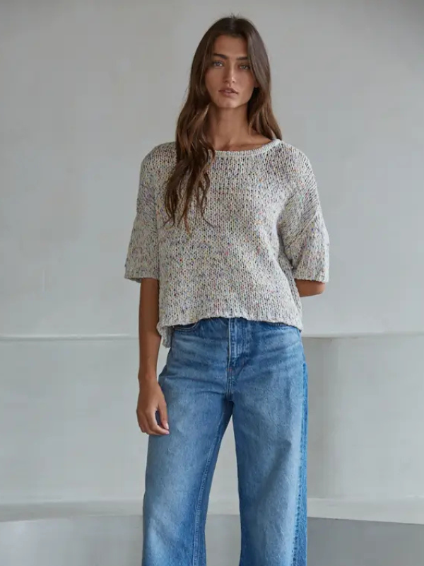 Woman wearing a patterned top and blue jeans against a plain background