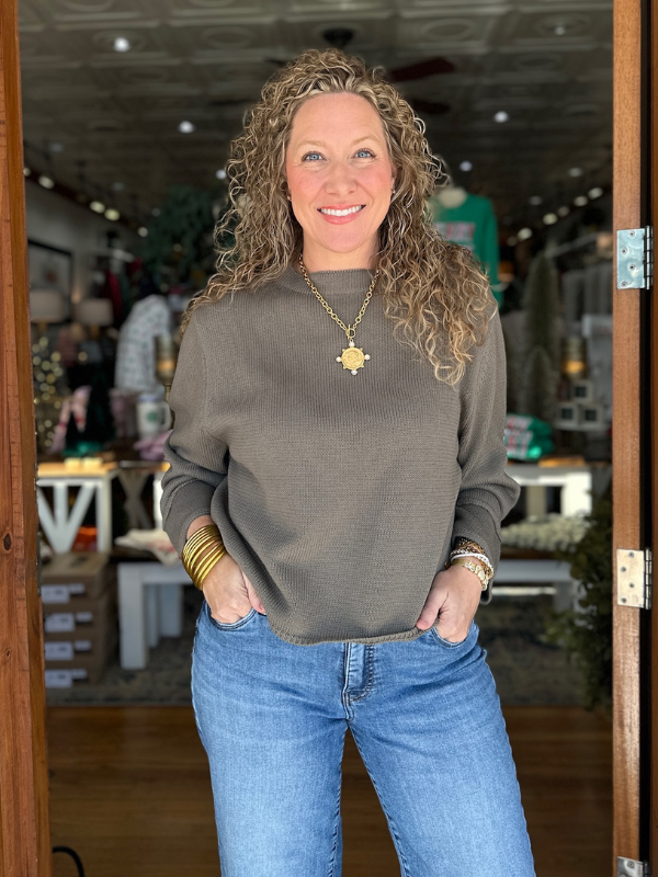 Woman wearing a gray sweater and blue jeans standing in a store.