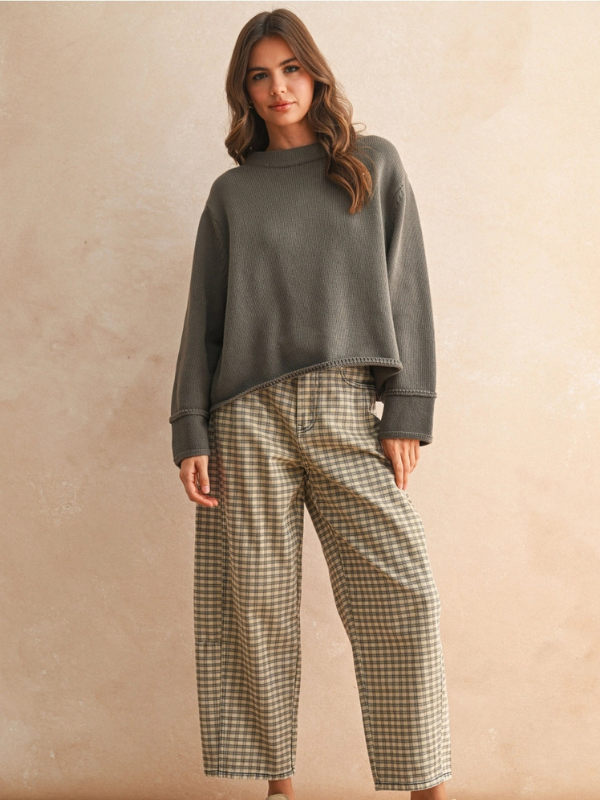 Woman wearing a gray sweater and plaid pants against a beige background