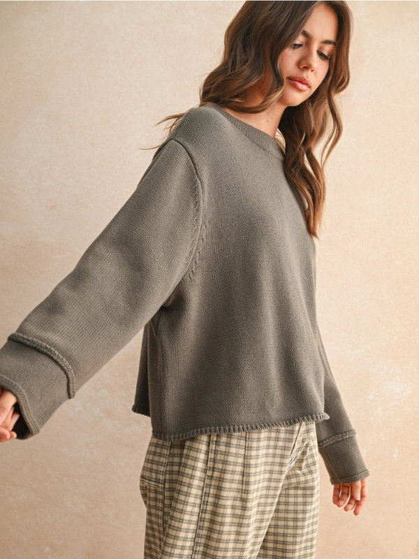 Woman wearing a gray sweater and plaid pants against a beige background