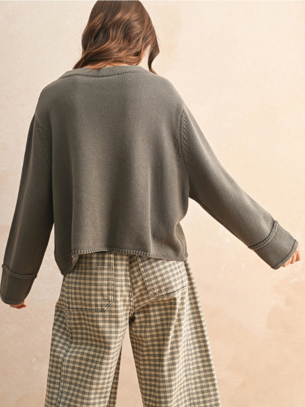 Person wearing a green sweater and plaid pants on a beige background