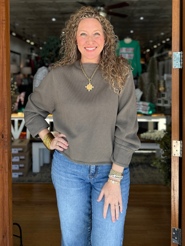 Woman wearing a gray sweater and blue jeans standing in a store.