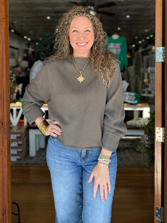 Woman wearing a gray sweater and blue jeans standing in a store.