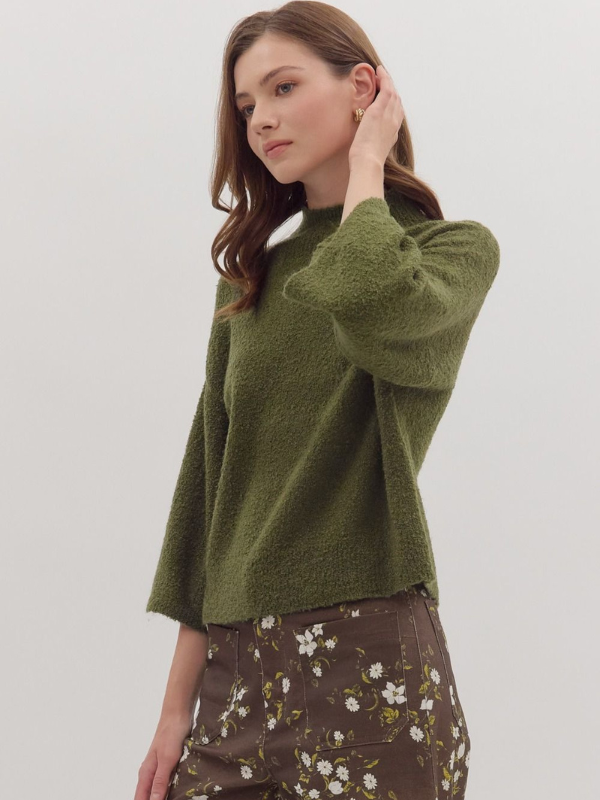 Woman wearing a green sweater and floral pants on a plain background