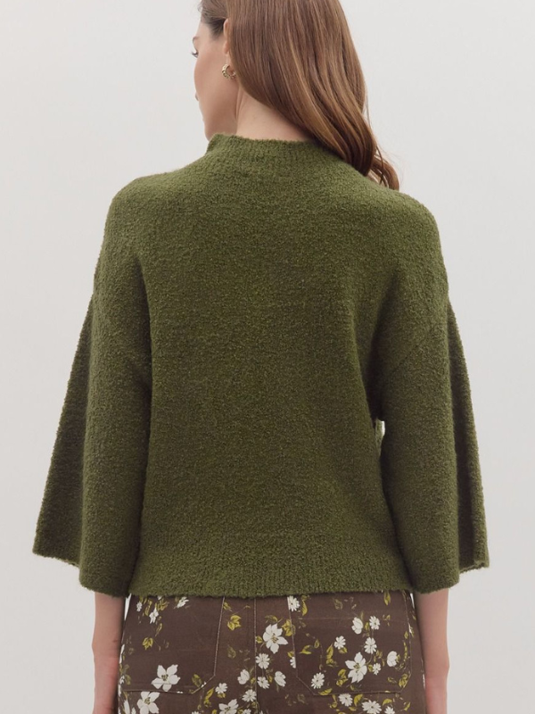 Woman wearing a green knitted sweater with a plain background
