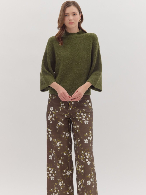 Woman wearing a green sweater and floral pants on a white background
