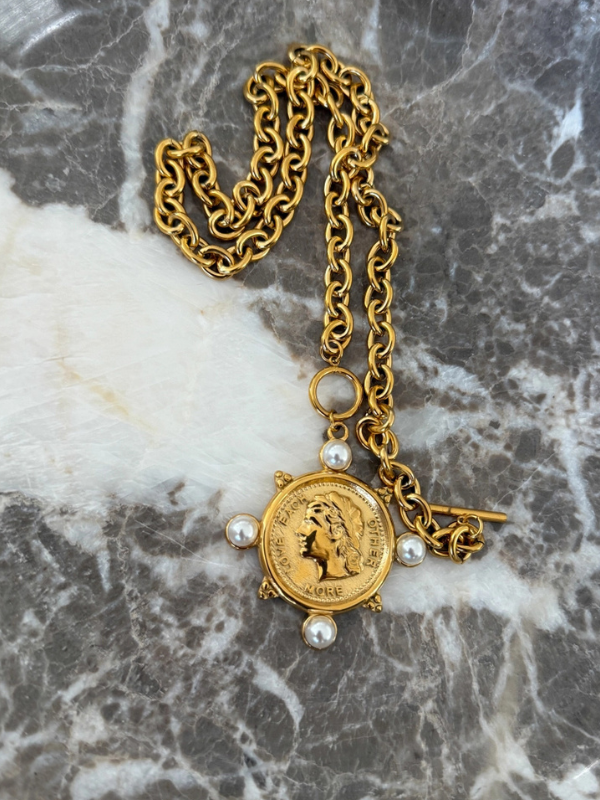Gold chain necklace with a coin pendant on a marble surface