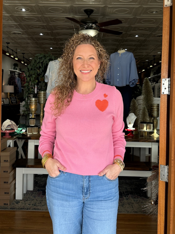 Woman wearing a pink sweater with a heart design in a store setting