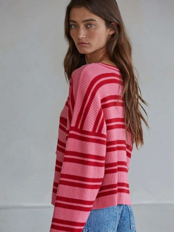 Woman wearing a pink and red striped sweater with blue jeans against a plain background