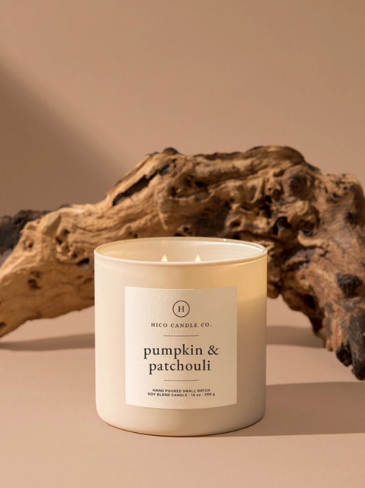 Candle labeled 'pumpkin & patchouli' from HICO CANDLE CO. on a neutral background with driftwood.