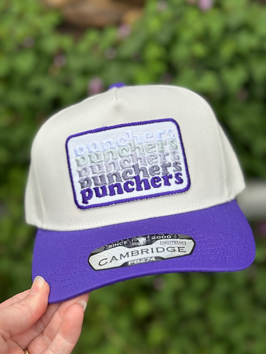 White and purple cap with 'punchers' text held against a green background