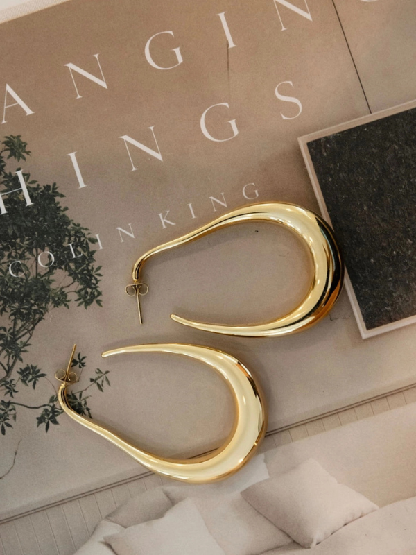 Gold hoop earrings on a surface with a 'Stranger Things' book in the background