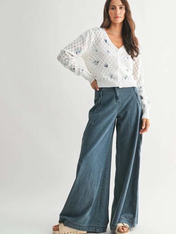 Woman wearing a white lace top and blue jeans on a plain background