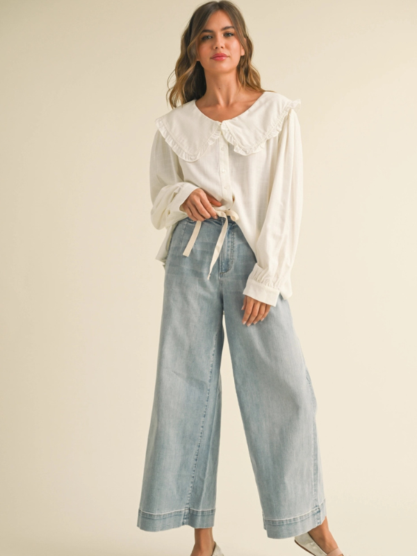 Woman wearing a white blouse with ruffled sleeves and light blue jeans on a beige background