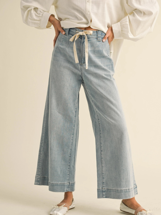 Light blue wide-leg jeans worn with a white top on a beige background
