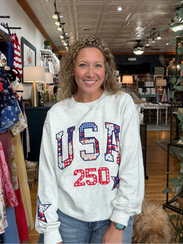 Woman wearing a white sweatshirt with 'USA 250' design in a store setting.