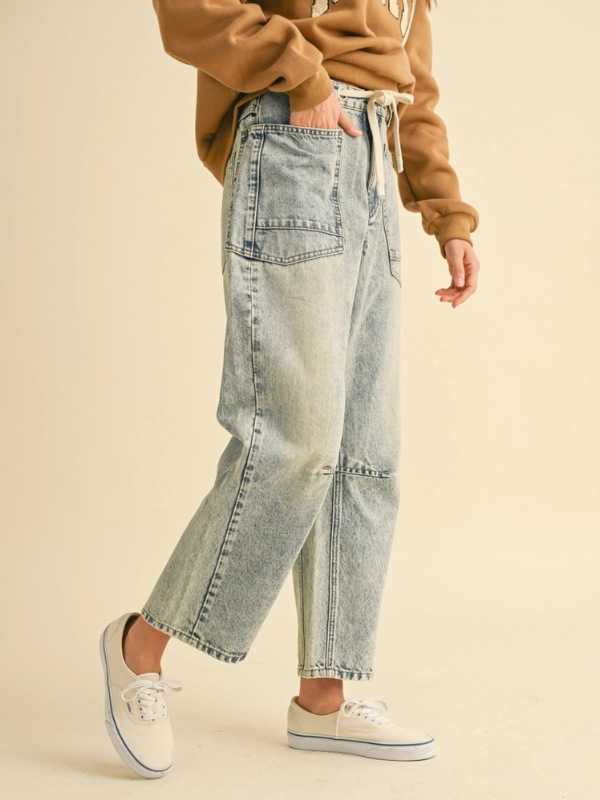 Person wearing light blue jeans and a brown sweater on a beige background
